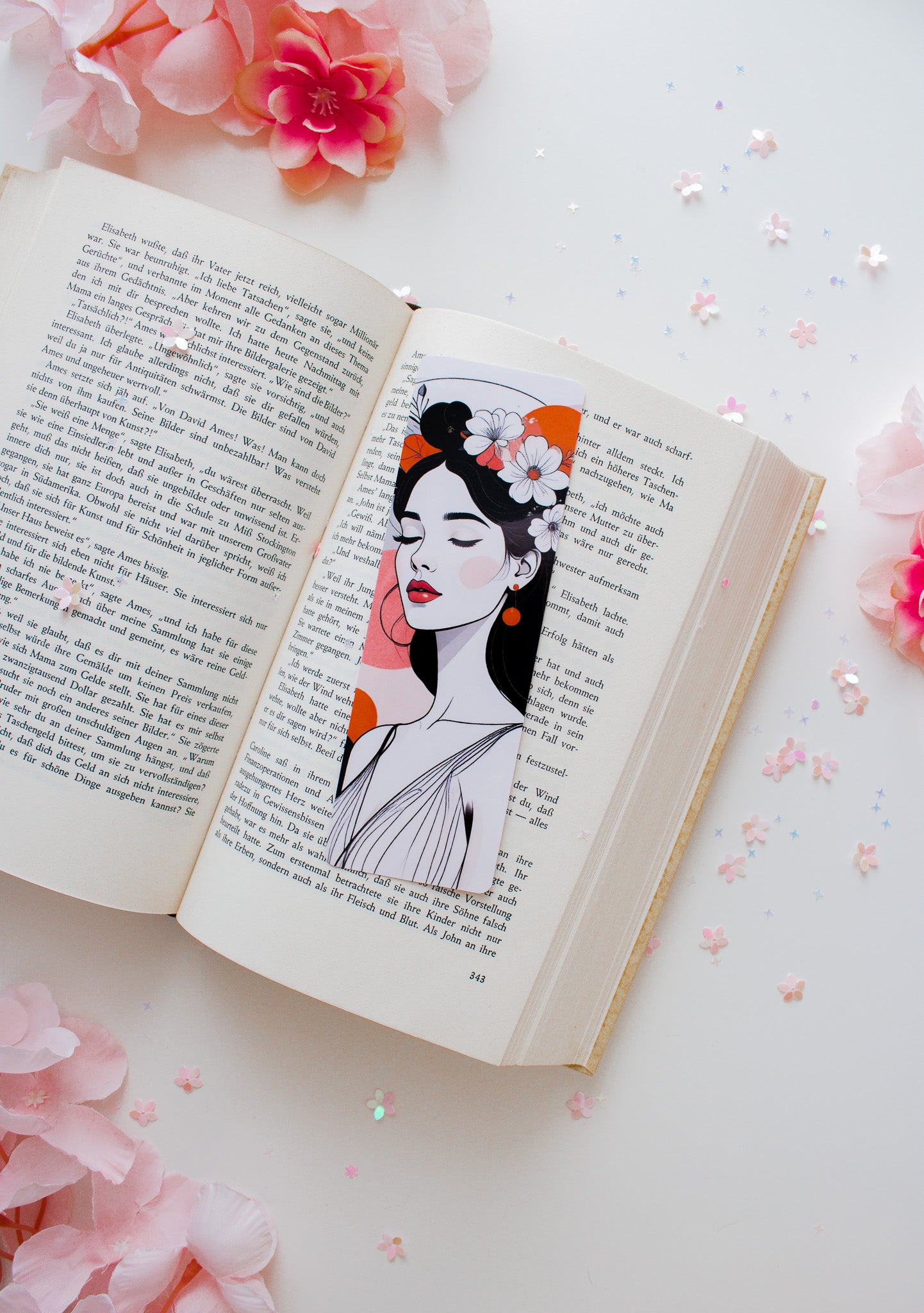 Laminiertes Lesezeichen Floral Woman mit weißen Blüten, roten Lippen und orangefarbenem Hintergrundakzent, auf aufgeschlagenem Buch mit rosa Blüten