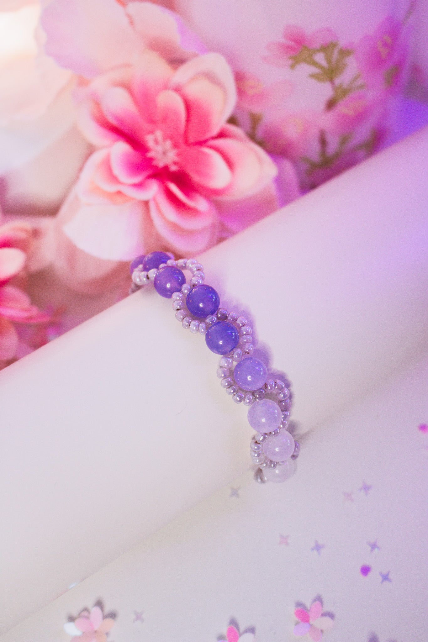 Nahaufnahme eines Perlenbandes mit milchig-weißen Acrylperlen und Silberperlen auf weißem Armband-Display vor lila Hintergrund