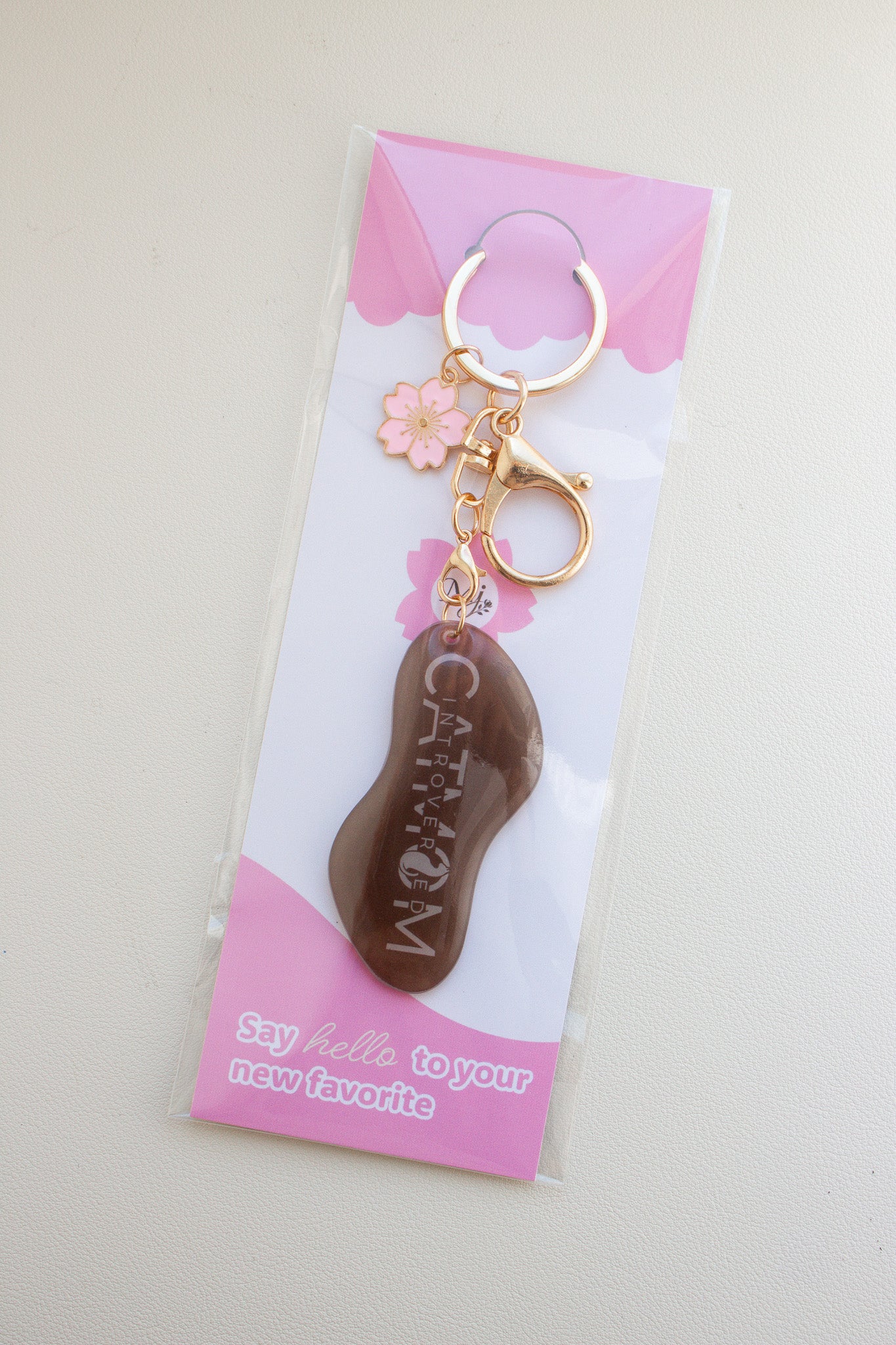 Brauner „Introverted Cat Mom" Schlüsselanhänger aus Schrumpffolie mit Resin-Versiegelung, pinkem Kirschblüten-Charm und goldfarbenem Karabiner, verpackt in transparenter Tüte mit pinker Brandingkarte
