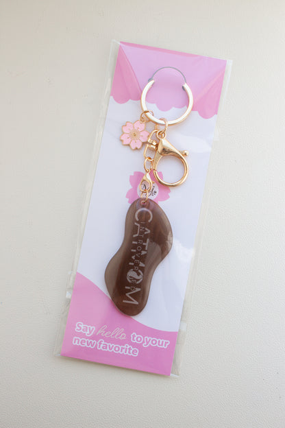 Brauner „Introverted Cat Mom" Schlüsselanhänger aus Schrumpffolie mit Resin-Versiegelung, pinkem Kirschblüten-Charm und goldfarbenem Karabiner, verpackt in transparenter Tüte mit pinker Brandingkarte
