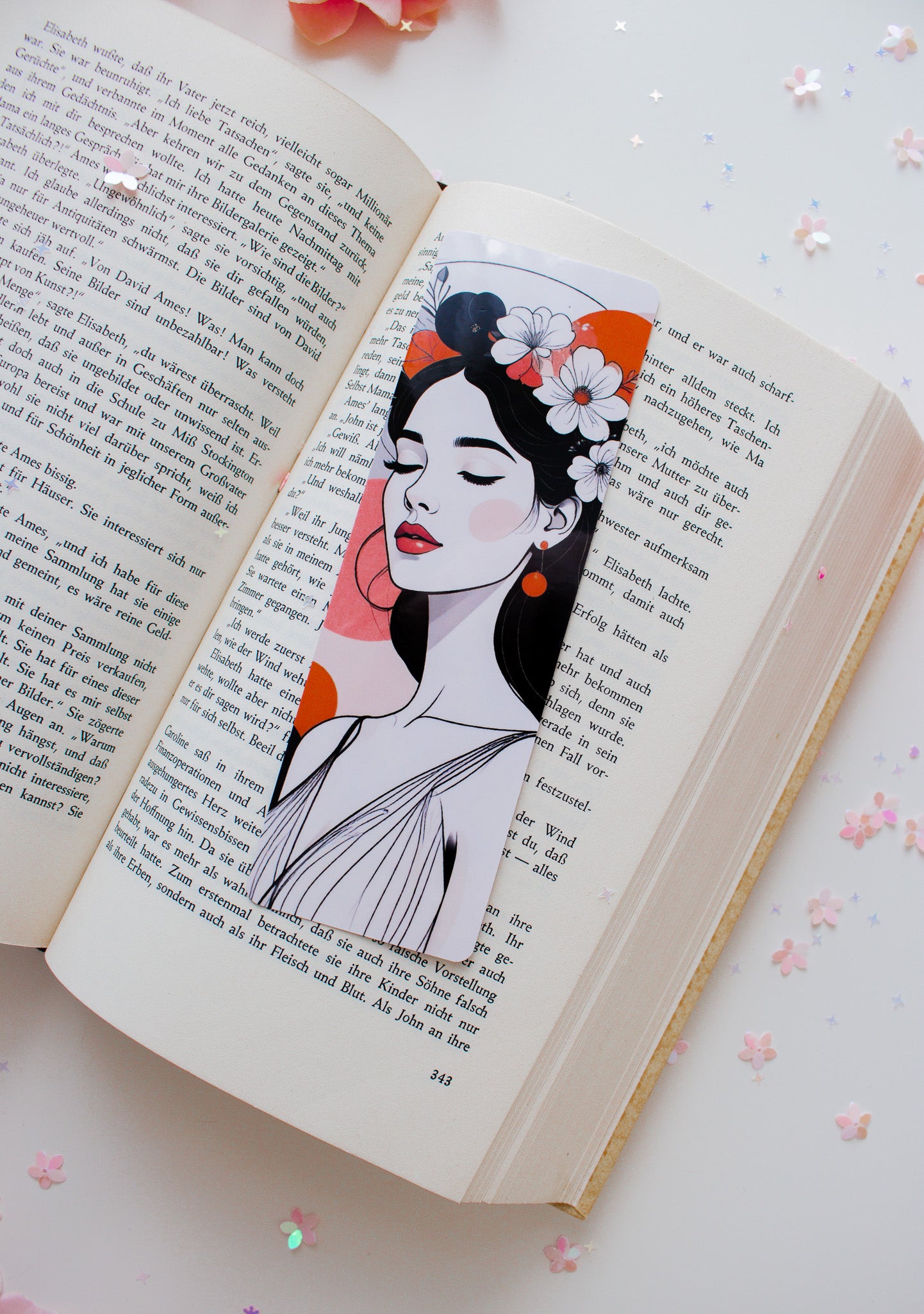 Doppelseitiges Glossy-Lesezeichen mit minimalistischer Frauenillustration, Blumenkranz, rote Lippen, orangefarbene Farbflächen, auf aufgeschlagenem Buch mit Sternenkonfetti

