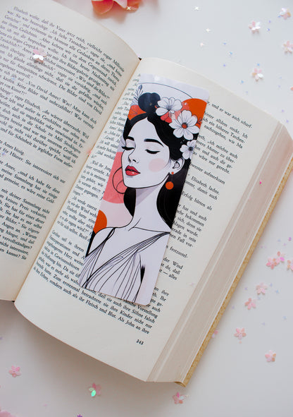 Doppelseitiges Glossy-Lesezeichen mit minimalistischer Frauenillustration, Blumenkranz, rote Lippen, orangefarbene Farbflächen, auf aufgeschlagenem Buch mit Sternenkonfetti

