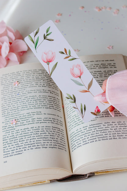 Doppelseitiges Lesezeichen mit Aquarell-Blumen-Motiv – rosa Tulpen und grüne Zweige auf weißem Hintergrund, gehalten über einem aufgeschlagenen Buch mit rosa Blütenblättern