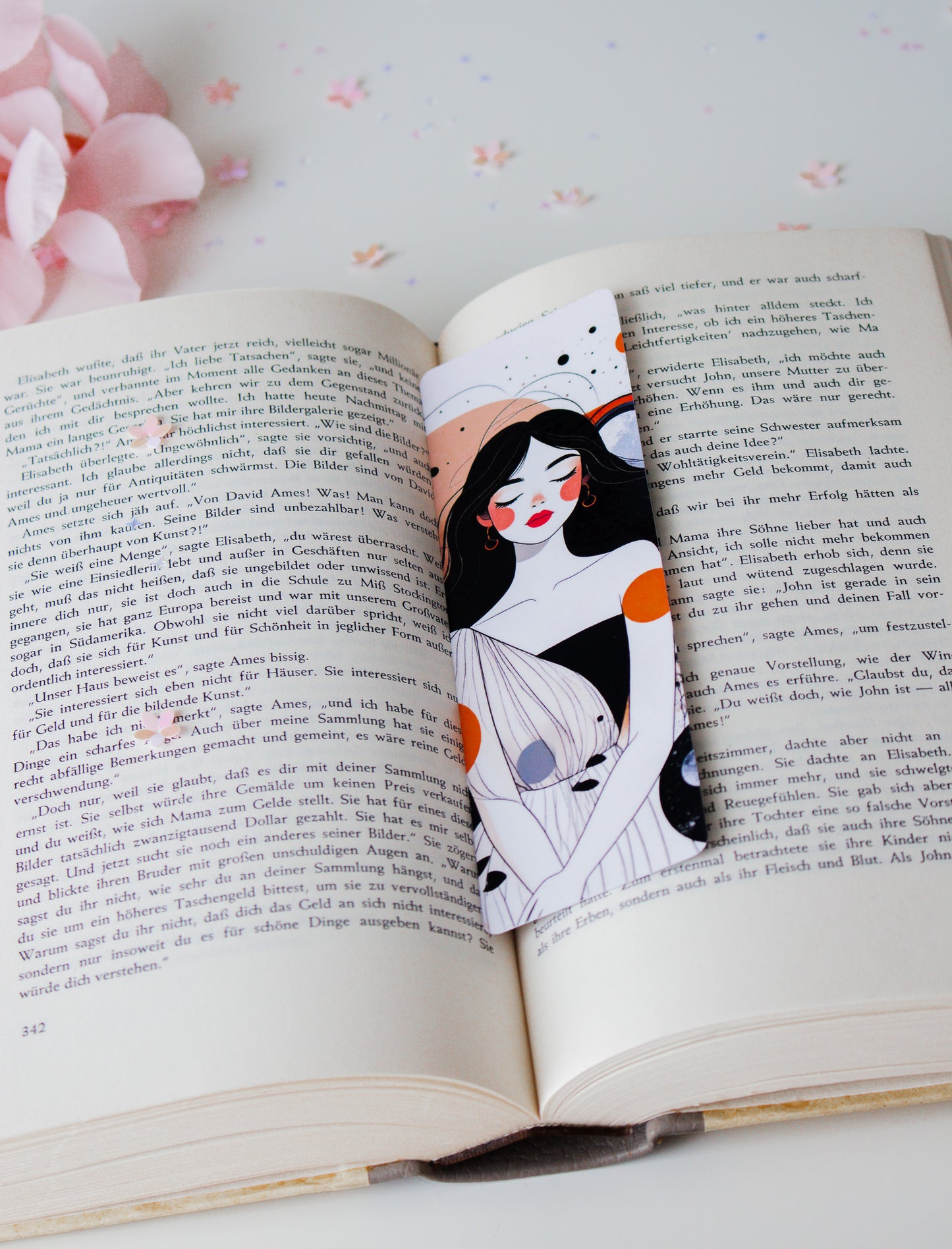 Doppelseitiges Lesezeichen mit minimalistischer Frauenillustration, abstrakte Farbakzente in Orange und Grau, auf aufgeschlagenem Buch mit rosa Blüten