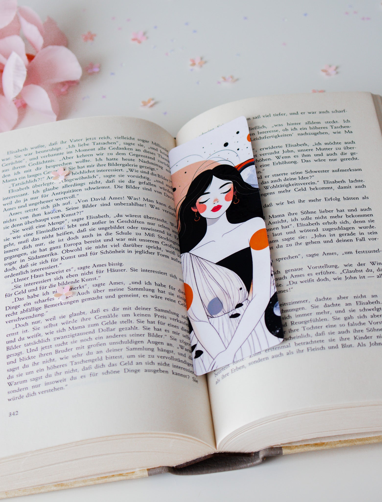 Doppelseitiges Lesezeichen mit minimalistischer Frauenillustration, abstrakte Farbakzente in Orange und Grau, auf aufgeschlagenem Buch mit rosa Blüten
