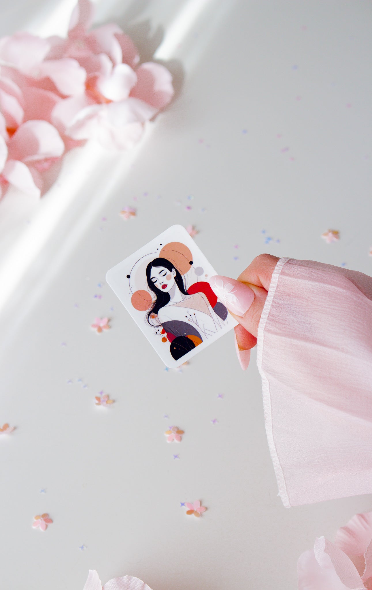 Eleganter Vinyl Sticker abstrakte Frau, schwarze Haare, rote Lippen, warme Erdtöne in Altrosa, Orange und Grau, in der Hand gehalten vor Sternenkonfetti