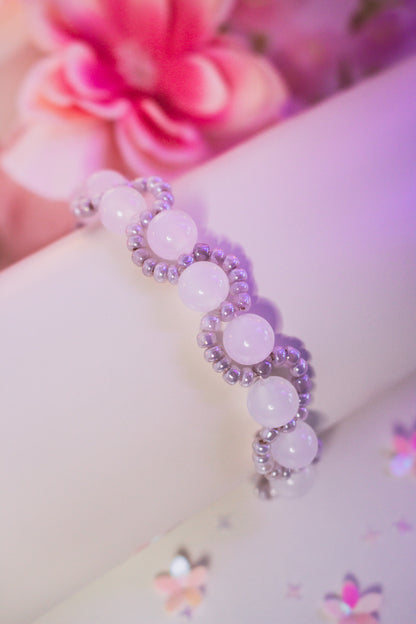 Perlenarmband mit dunkelvioletten und helllila Acrylperlen und Silberperlen, auf weißem Armband-Display vor rosa Blumendekoration