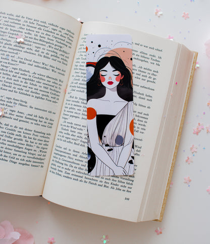 Laminiertes Lesezeichen mit abstrakter Celestial-Woman-Illustration – Frau mit roten Lippen, orangefarbenen und grauen Akzenten, aufgeschlagen im Buch mit Konfetti