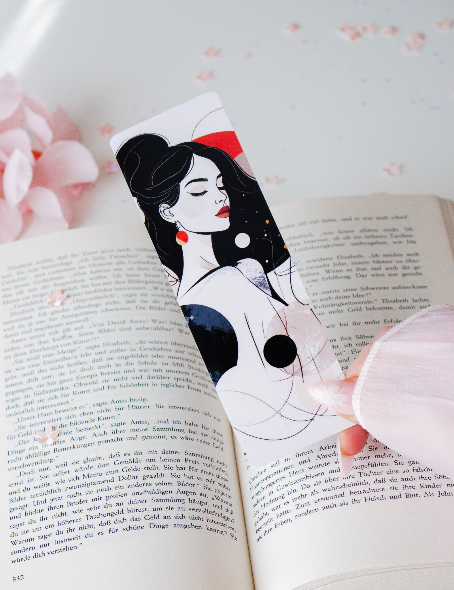 Laminiertes Lesezeichen mit eleganter Frauenillustration, schwarze Hochsteckfrisur, rotes Haarband und rote Ohrringe, schräg in aufgeschlagenem Buch mit rosa Blüten