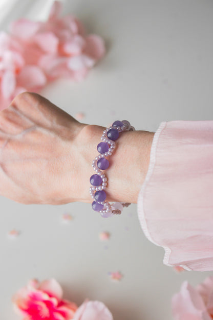 Elegantes Perlenarmband mit dunkelvioletten Acrylperlen und Silberperlen am Handgelenk, vor hellem Hintergrund mit Rosenblütenblättern