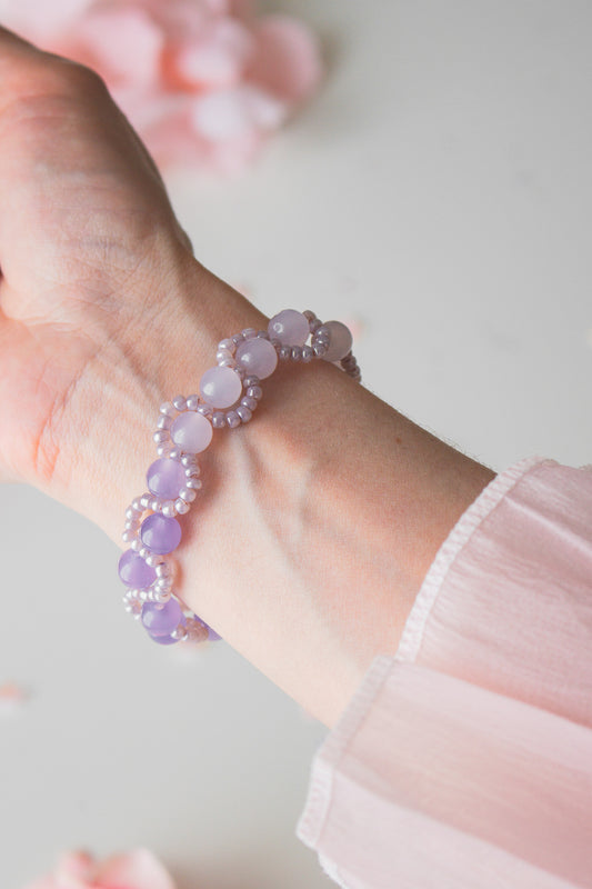 Zartes Perlenarmband mit helllila Acrylperlen und Silberperlen am Handgelenk, vor hellem Hintergrund mit Rosenblütenblättern