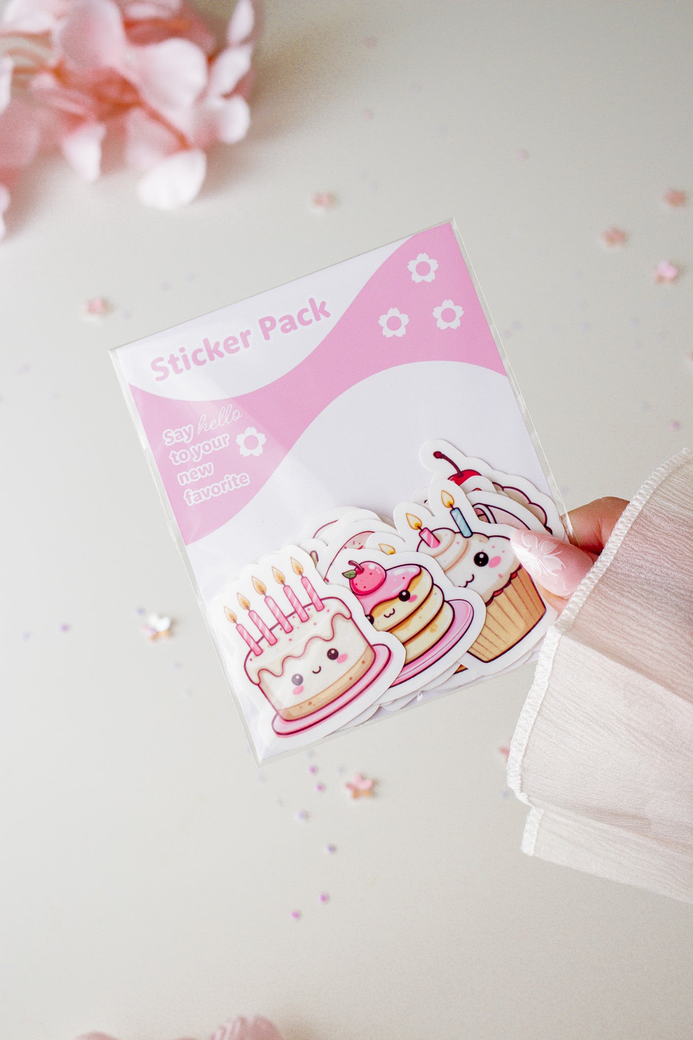 Hand hält ein kawaii Sticker Pack mit drei süßen Dessert-Stickern – Geburtstagstorte, Pancake und Cupcake – in Rosa und Weiß, Detailansicht
