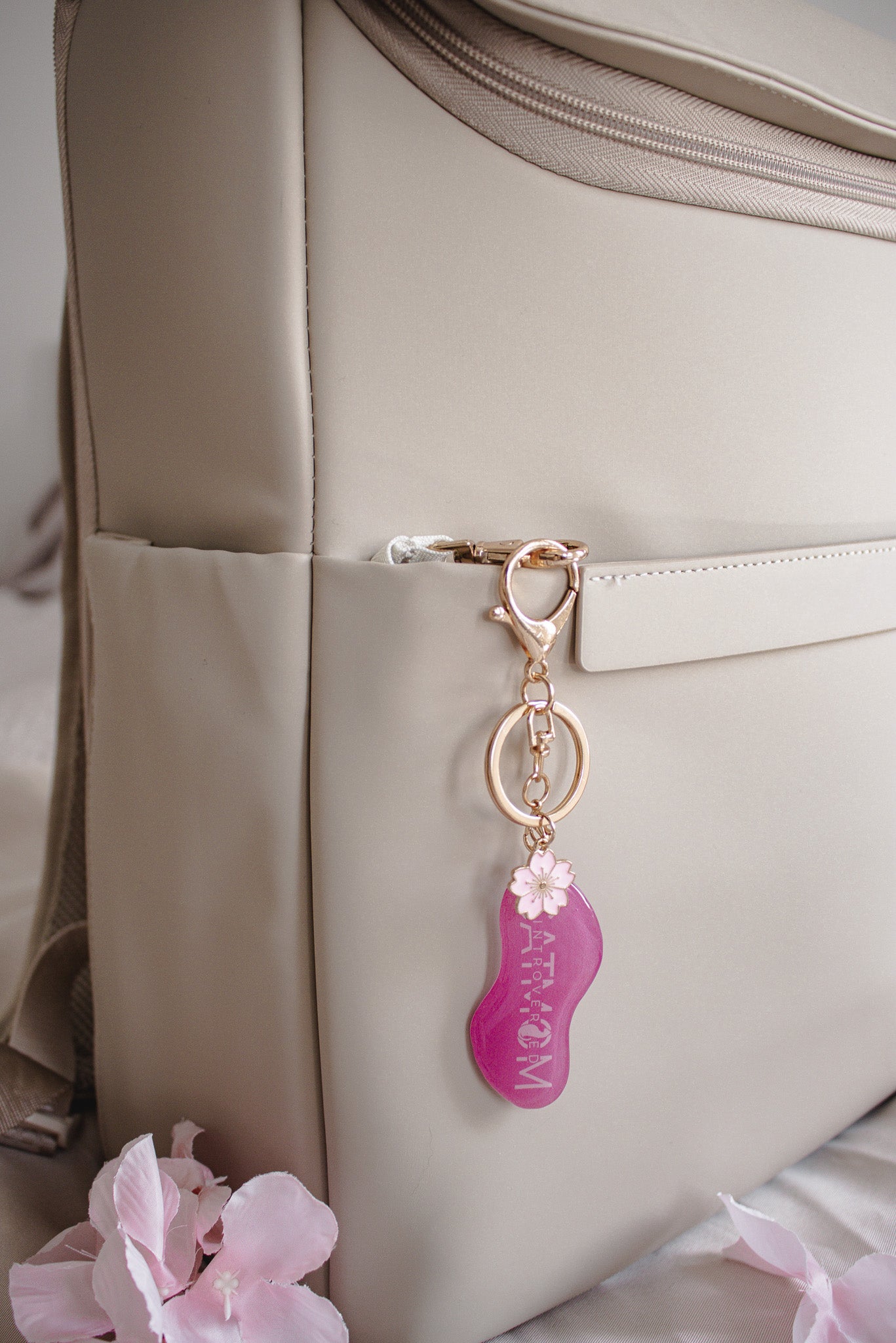 Pinker „Cat Mom" Schlüsselanhänger mit Kirschblüten-Detail und goldfarbenem Karabiner, hängend an einer beigen Tasche mit rosa Blüten im Hintergrund
