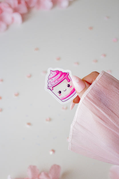 Kawaii Eiscreme-Sticker in Pink mit süßem Gesicht, gehalten von einer Hand vor hellrosa Hintergrund mit Blütenblättern
