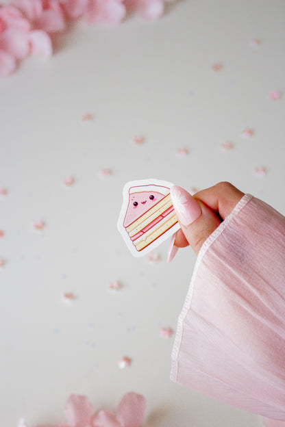 Kawaii Torte Sticker in Rosa, gehalten von einer Hand vor hellrosa Hintergrund mit Blütenblättern