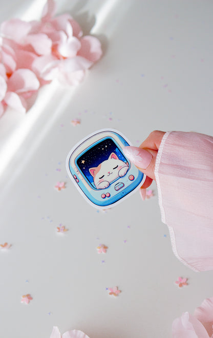 Kawaii Vinyl Sticker Space Cat, schlafendes weißes Kätzchen im Retro-Pet-Gerät mit Sternenhimmel, in der Hand gehalten vor rosa Blüten und Sternenkonfetti