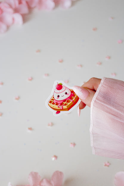 Kawaii Waffel Sticker mit Erdbeere, gehalten von einer Hand vor hellrosa Hintergrund