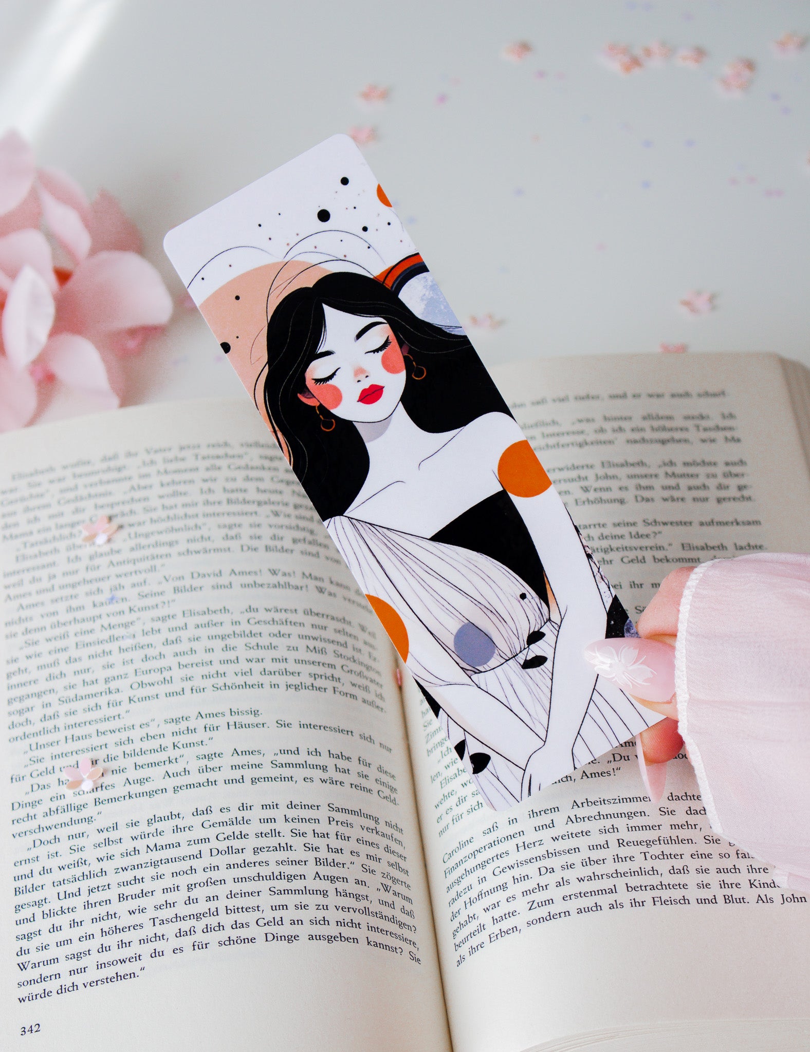 Laminiertes Lesezeichen mit abstrakter Illustration einer Frau mit roten Lippen, schwarzen Haaren und orangefarbenen Akzenten, gehalten über aufgeschlagenem Buch