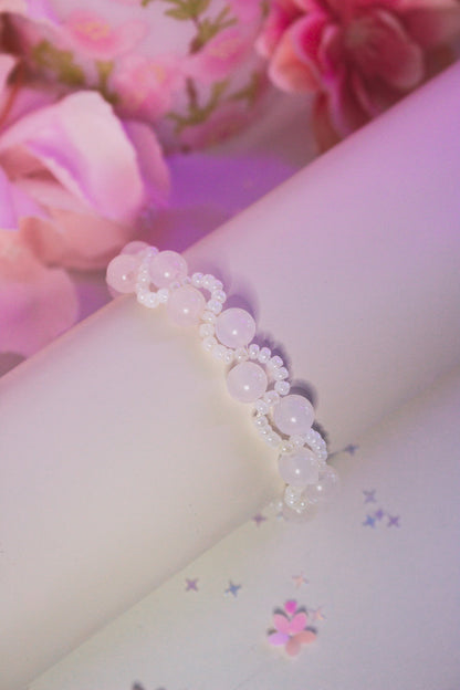 Nahaufnahme eines handgefertigten Armbands mit UV-Acrylperlen in Weiß und Rosa auf weißem Hintergrund mit Blumen