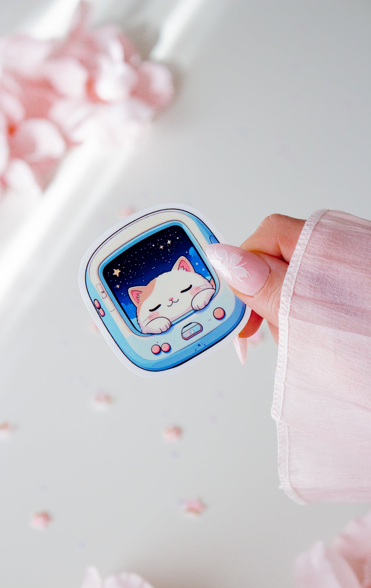 Niedlicher Space Cat Vinyl Sticker in der Hand gehalten, schlafende kawaii Katze im hellblauen Retro-Pet-Gerät mit Sternenhimmel, vor rosa Blüten