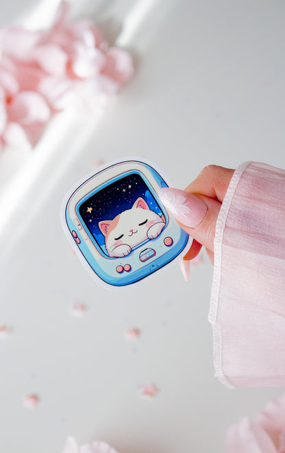 Niedlicher Space Cat Vinyl Sticker in der Hand gehalten, schlafende kawaii Katze im hellblauen Retro-Pet-Gerät mit Sternenhimmel, vor rosa Blüten