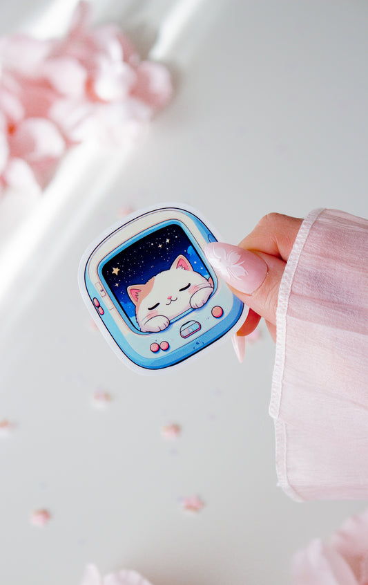 Niedlicher Space Cat Vinyl Sticker in der Hand gehalten, schlafende kawaii Katze im hellblauen Retro-Pet-Gerät mit Sternenhimmel, vor rosa Blüten