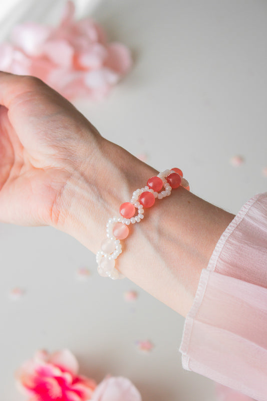 Perlenarmband mit korallenroten und weißen Acrylperlen am Handgelenk, vor hellem Hintergrund mit rosa Blütenblättern
