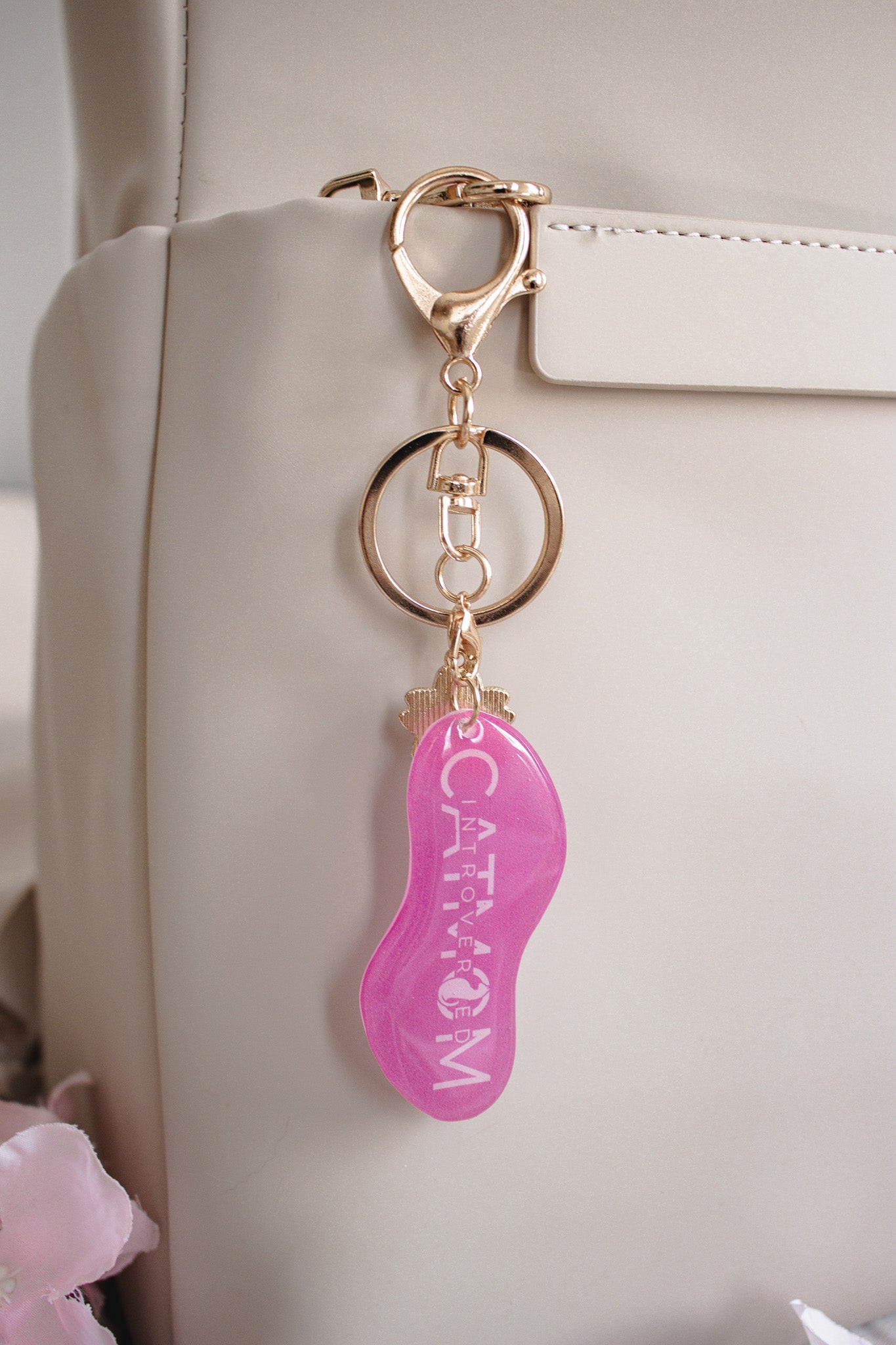 Pinker Schlüsselanhänger „Introverted Cat Mom" aus Schrumpffolie mit Resin-Versiegelung, goldfarbenem Karabinerhaken und Schlüsselring, hängend an einer beigen Handtasche
