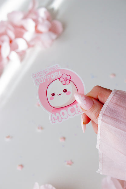 Runder Vinyl Sticker Emotional Support Mochi, niedliches weißes Mochi mit Kirschblüte und rosigen Wangen auf rosa Hintergrund, in der Hand gehalten vor rosa Blüten