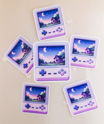 Sechs kawaii Retro-Handheld-Konsolen-Sticker in Lila mit Pixel-Art-Cottage und Mondnacht-Szene, Draufsicht auf beigem Hintergrund mit Sternenkonfetti

