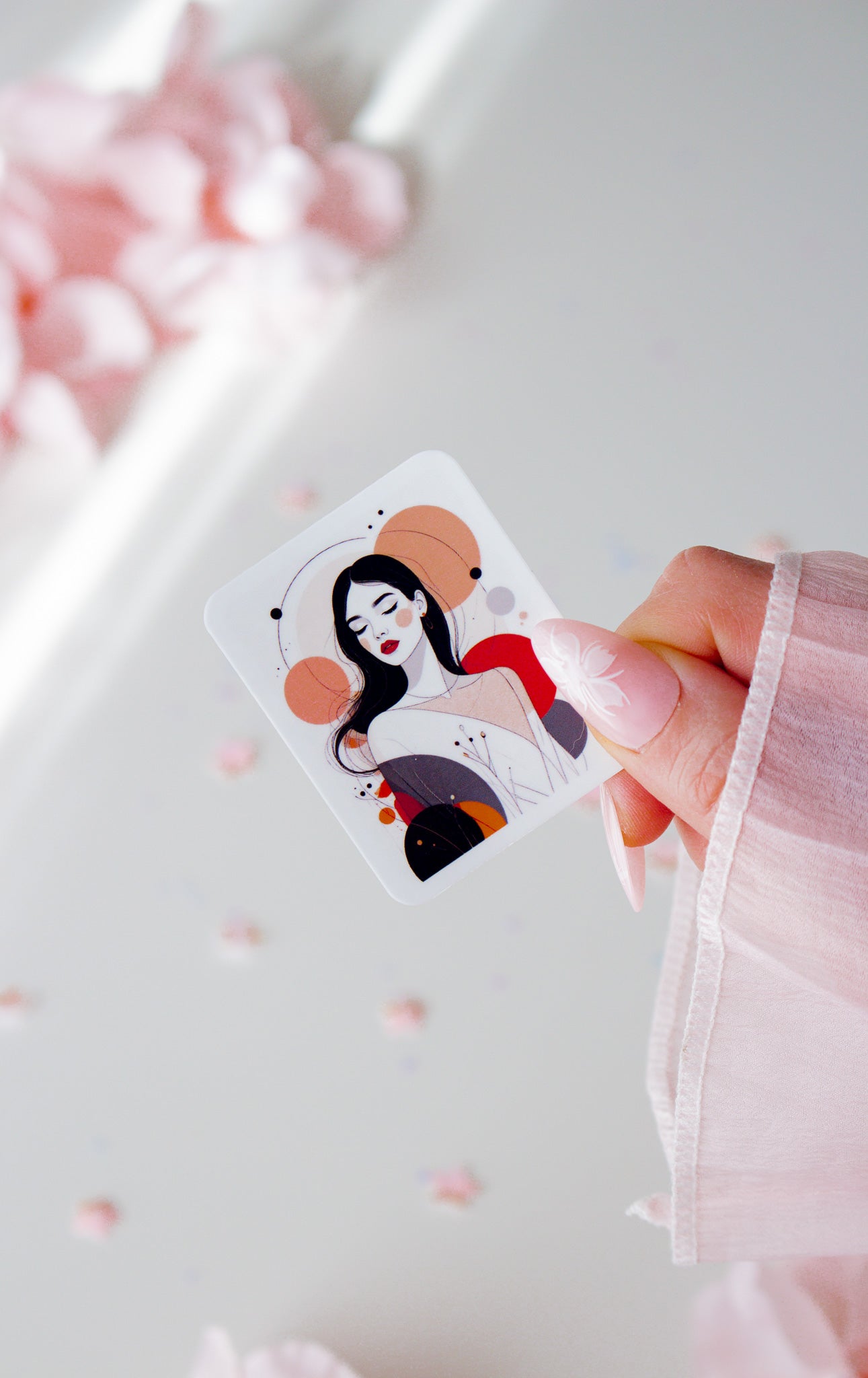 Vinyl Sticker mit eleganter Frauenillustration, schwarze lange Haare, rote Lippen, abstrakte Kreise in Altrosa, Rot, Orange und Schwarz, in der Hand gehalten vor rosa Blüten